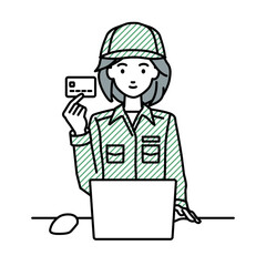 デスクで座ってPCを使いながらクレジットカードを手に持っている作業員の女性