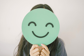 Happy mixed Asian girl  holding smile emoji face, positive mental health concept - obrazy, fototapety, plakaty