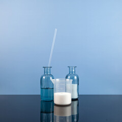 White water-soluble powder in flask and collagen serum on blue background. L-carnitine concentrate...