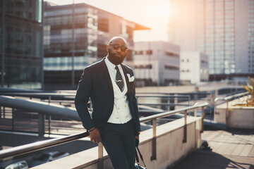 A confident mature bald bearded African man entrepreneur in sunglasses and a tailored suit is...