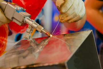 Welder hands using portable handheld laser welding machine with sparks - close up. Manufacturing, industrial, equipment, technology and metalworking concept - obrazy, fototapety, plakaty