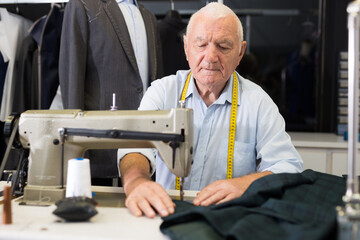Portrait of elderly man tailor working on sewing machine at studio