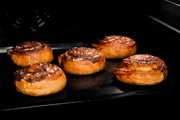 Five baked cinnamon buns on tray in electric oven. Swedish cuisine, homemade bakery, food, cooking and pastry concept