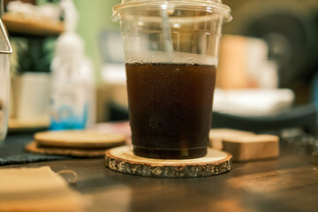 selective focus, glass of Iced black coffee in coffee shop. cold americano coffee in plastic cup on wooden table in cafe with sunlight background