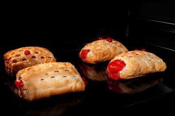 Four baked puff pastry buns with red strawberry jam on tray in electric oven. Homemade bakery, food, cooking and pastry concept