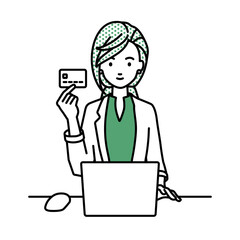 デスクで座ってPCを使いながらクレジットカードを手に持っているジャケットの女性