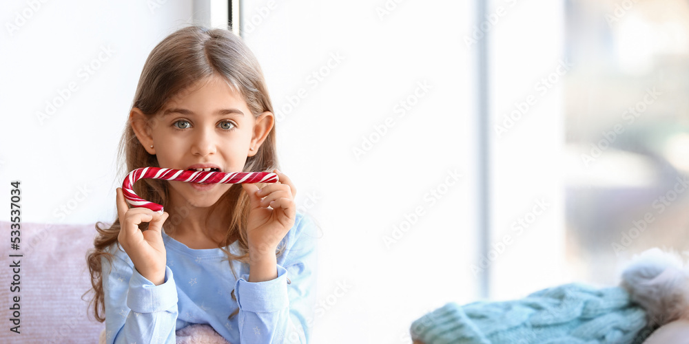 Poster Cute little girl with Christmas candy cane near window