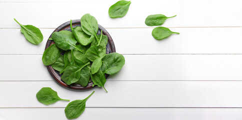 Plate of fresh spinach on white wooden background with space for text