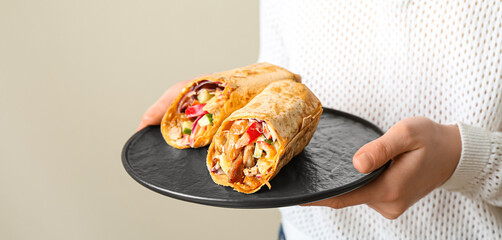 Woman holding plate with tasty doner kebabs on light background, closeup