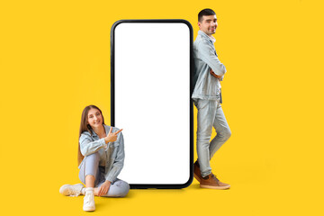 Young couple and big smartphone with blank screen on yellow background