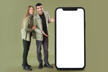 Young couple near big smartphone with blank screen on color background