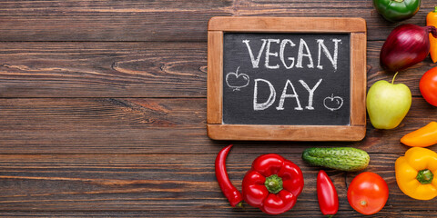 Chalkboard with text VEGAN DAY and fresh products on wooden background with space for text