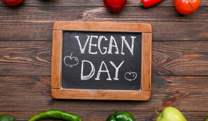 Chalkboard with text VEGAN DAY and fresh products on wooden background