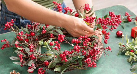 Woman making beautiful Christmas wreath with mistletoe at table, closeup