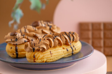 Eclairs cakes with chocolate cream and chocolate bar on brown background.Sweets and desserts. Baked...