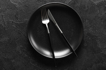 Black plate, knife and fork on dark background