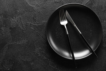 Black plate, knife and fork on dark background, top view