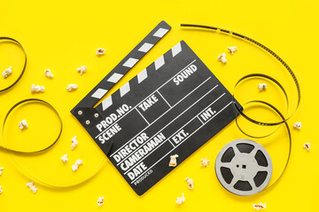 Movie clapper with reel and popcorn on yellow background