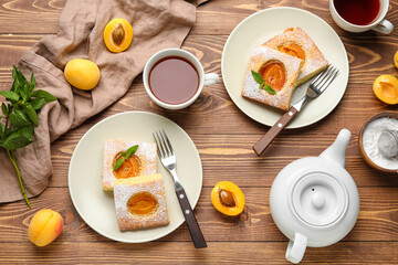 Plates with tasty apricot pie, cup of tea and teapot on wooden background