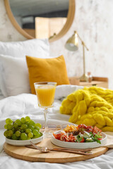 Wooden tray with tasty breakfast on bed