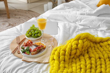 Tray with tasty breakfast and eyeglasses on bed