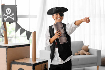 Little boy dressed as pirate playing with map and cardboard ship at home