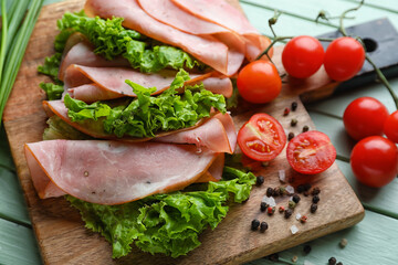 Board with slices of tasty ham, lettuce and tomatoes on color wooden table, closeup