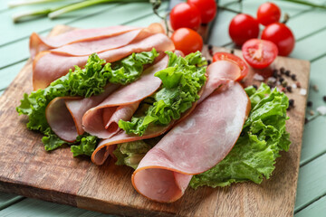 Board with slices of tasty ham and lettuce on color wooden table, closeup