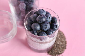 Glass with delicious chia seed pudding and blueberry on pink background, closeup