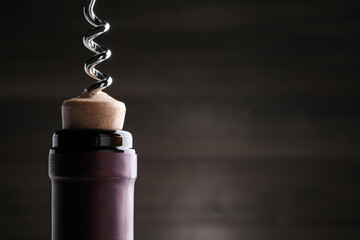 Opening wine bottle with corkscrew on dark background, closeup. Space for text