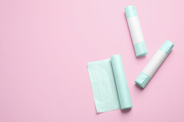 Rolls of garbage bags on pink background, flat lay. Space for text