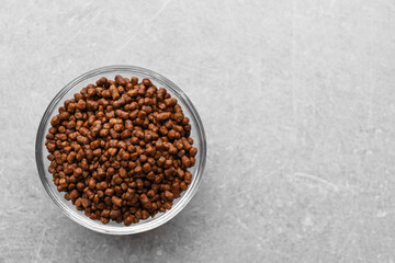 Buckwheat tea granules in glass bowl on light grey table, top view. Space for text
