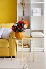 Pumpkin with beautiful flowers on table in bright living room