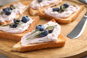 Tasty sandwiches with cream cheese, rosemary and berries on wooden tray, closeup