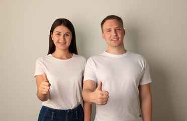 Fototapeta premium Portrait of happy young woman and man showing thumbs up on light background