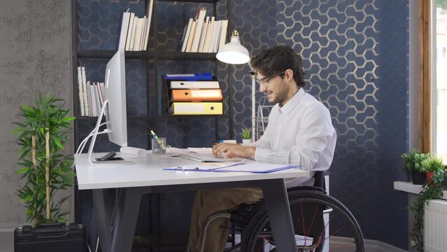 Disabled businessman sitting in wheelchair rejoicing and working in office.
Rejoicing disabled businessman looking at his computer.
