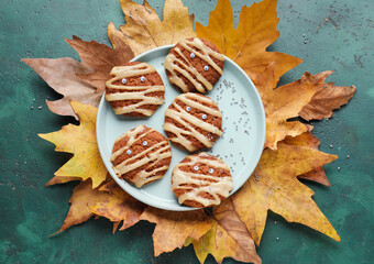 Plate with Halloween mummy cookies and fallen leaves on grunge background