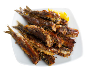 Grilled on fire sardines served with slice of lemon on white plate, traditional andalusian dish. Isolated over white background