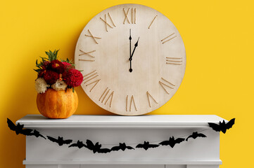 Vase with flowers and big clock on mantelpiece near yellow wall