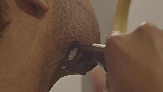 Close up of man using trimmer to shave his face while light flares in the camera lens