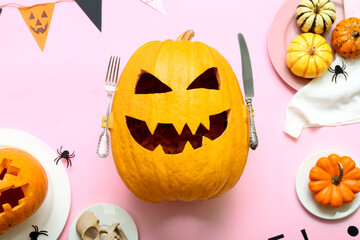 Plates with carved Halloween pumpkins and decor on pink background