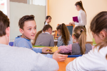 Happy pupils chattering sitting on back desks at lesson in elementary school