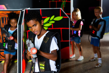 Portrait of happy cheerful preteen boy with laser pistol posing in laser tag labyrinth
