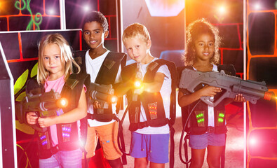 Joyful teens aiming laser guns at other players during lasertag game in dark room