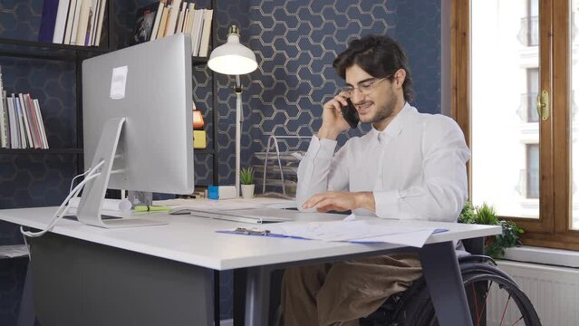 Disabled office worker sitting in a wheelchair and talking on the phone.
A worker sitting in a wheelchair is happy in the office and enjoys working.
