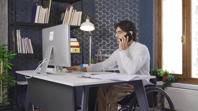 Disabled office worker sitting in a wheelchair and talking on the phone.
A worker sitting in a wheelchair is happy in the office and enjoys working.
