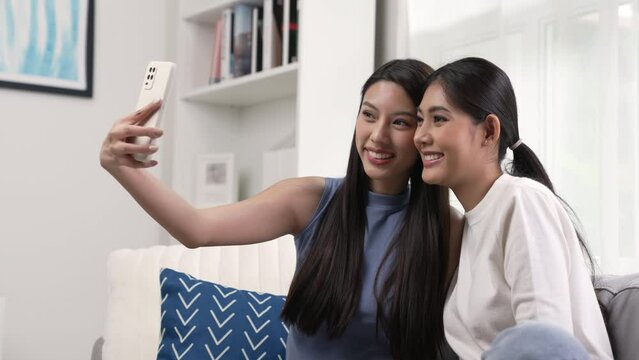 Happy young Asian lesbian couple taking selfie in the living room. LGBT couple lifestyle concept.