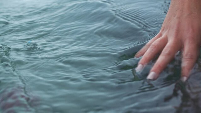 Manicure hand of woman touch water in sea, river or lake with calm waves in nature for peace, relax and freedom. Girl or female person touching ocean liquid on tropical beach holiday vacation trip