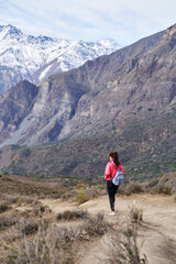 Fototapeta premium young woman with red jacket and backpack, descending the mountain in the middle of the Andes Mountains of Chile