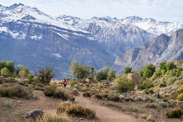 young woman with red jacket and backpack, descending the mountain in the middle of the Andes Mountains of Chile